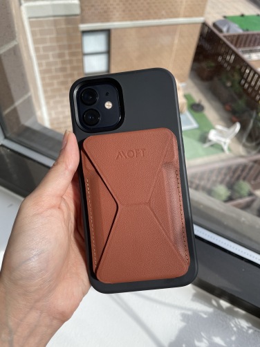 A brown faux leather phone wallet attached via magnets to the back of an iPhone 12 in a black case.