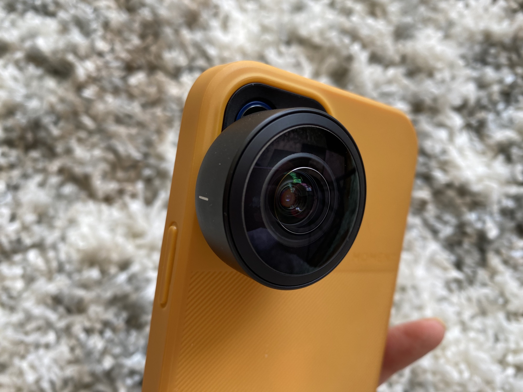 An iPhone 12 in a yellow case with an additional, large camera lens attached over the phone's camera. 