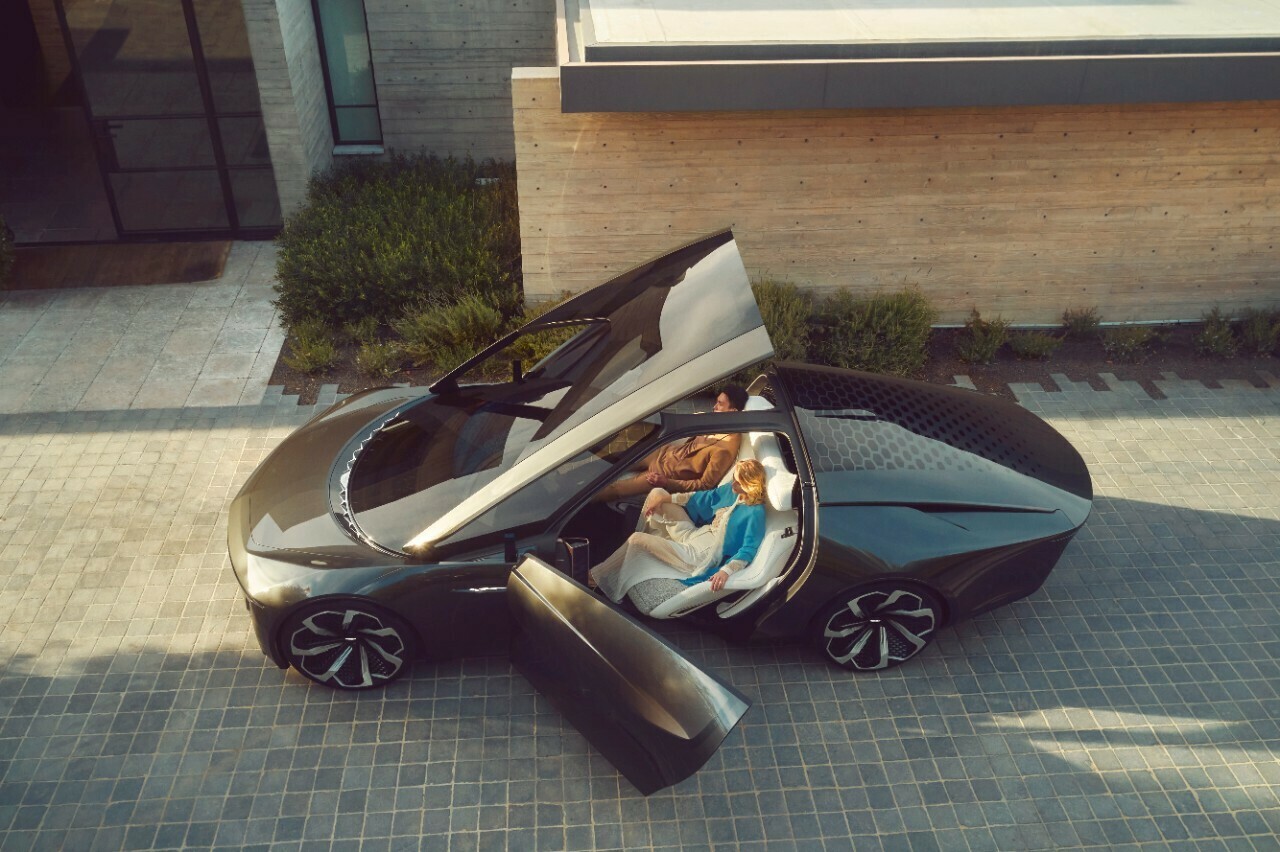 Gray car with roof and door open to reveal no steering wheel and two plush seats.