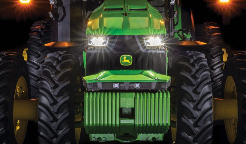 A close-up of the front end of a large tractor with its headlights on.