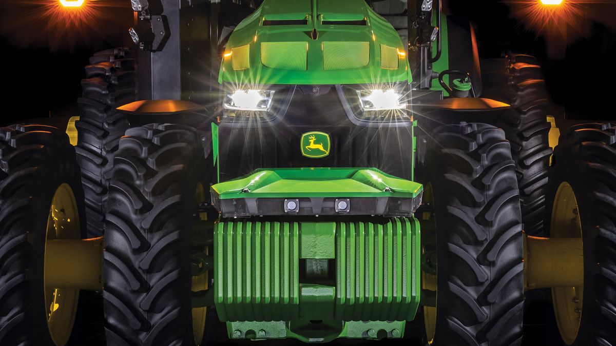 A close-up of the front end of a large tractor with its headlights on.