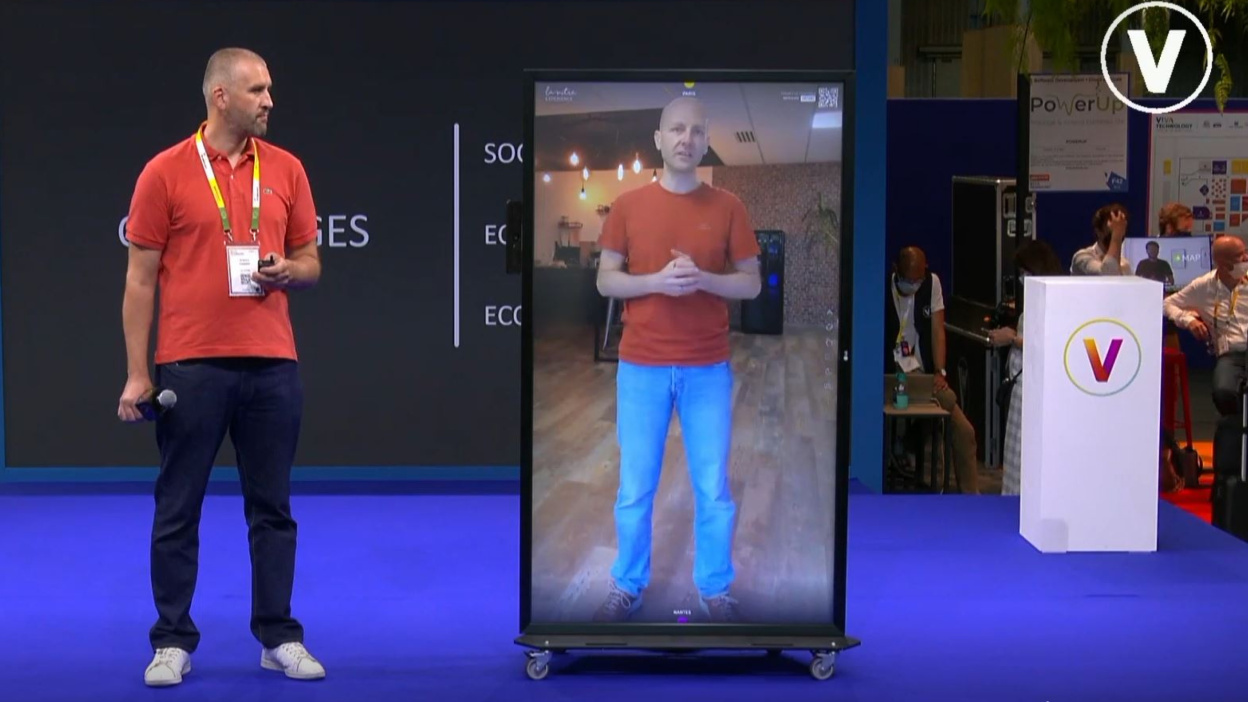 A person standing next to a mirror-like screen, communicating with another person in the screen.