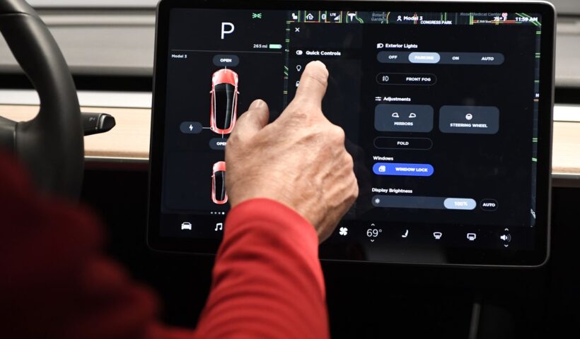 A driver with their hand touching the Tesla screen beside the car’s steering wheel.