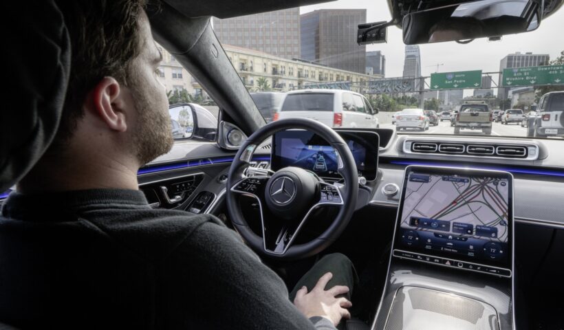 A man sits in the drivers seat of a Mercedes-Benz, showing off autonomous driving.