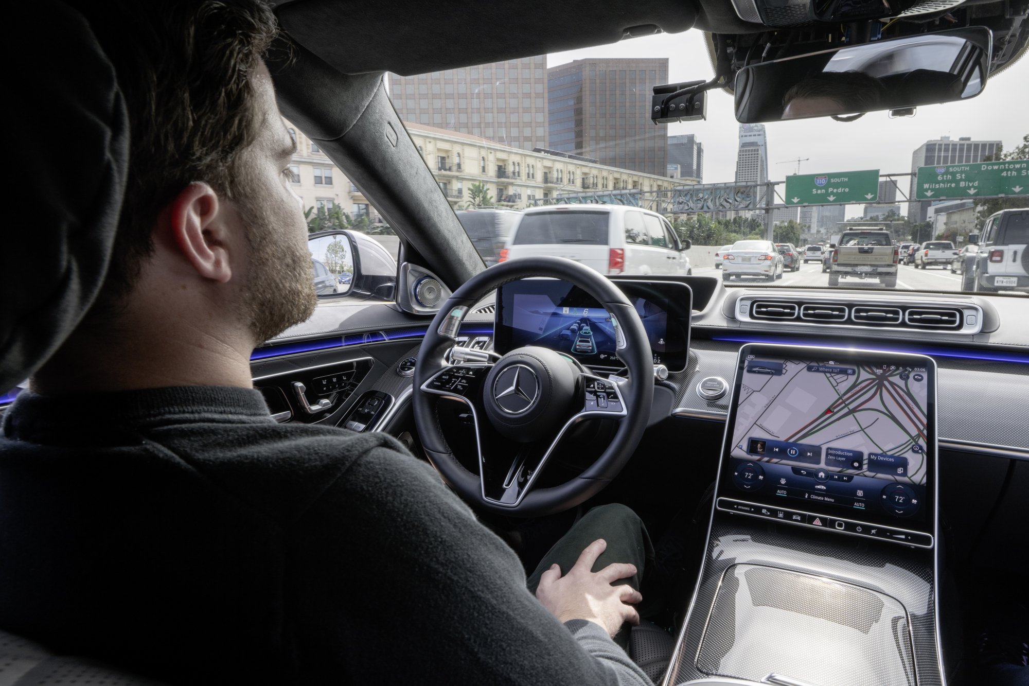 A man sits in the drivers seat of a Mercedes-Benz, showing off autonomous driving.