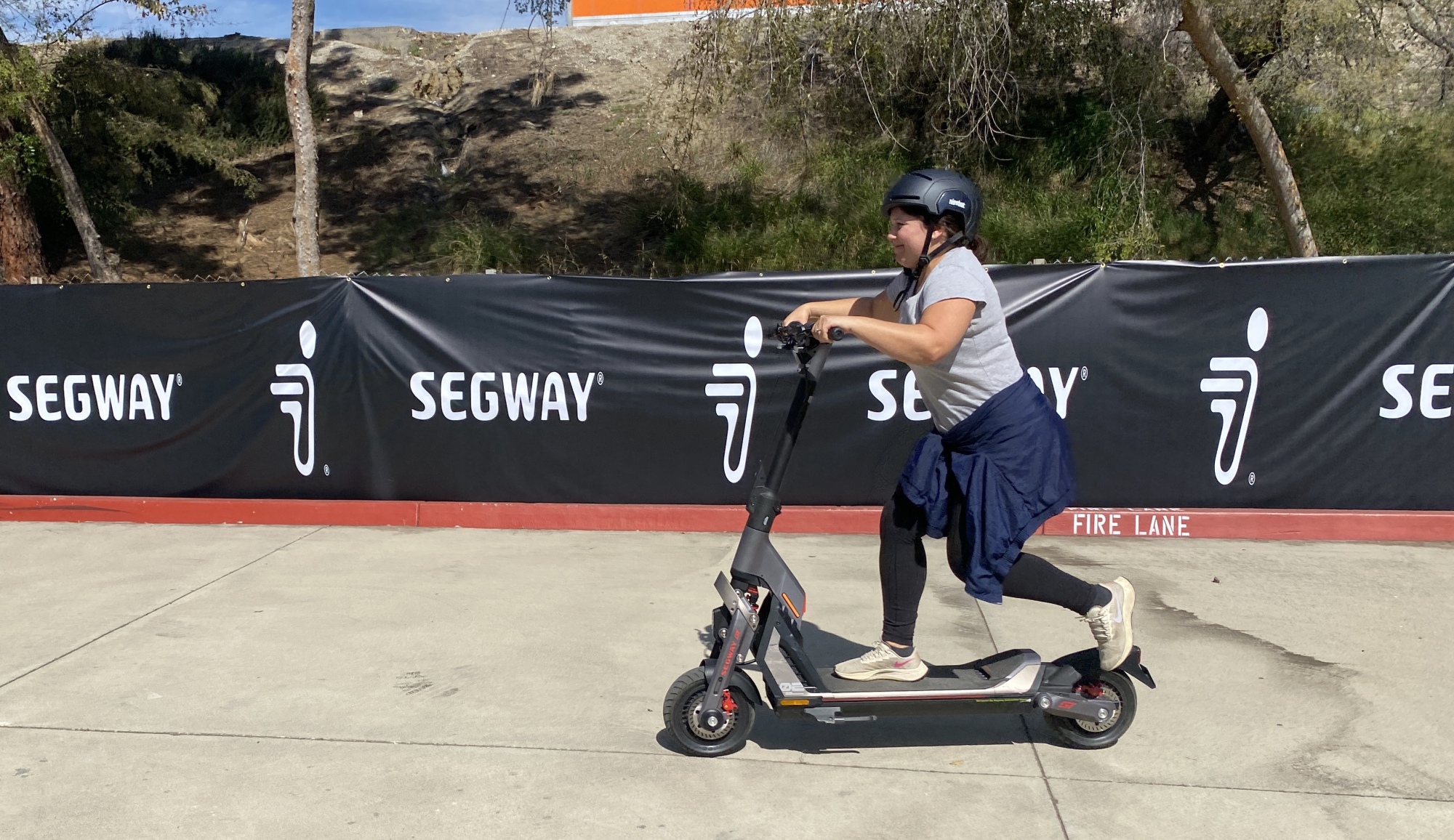 Mashable reporter riding an e-scooter in front of a Segway sign.