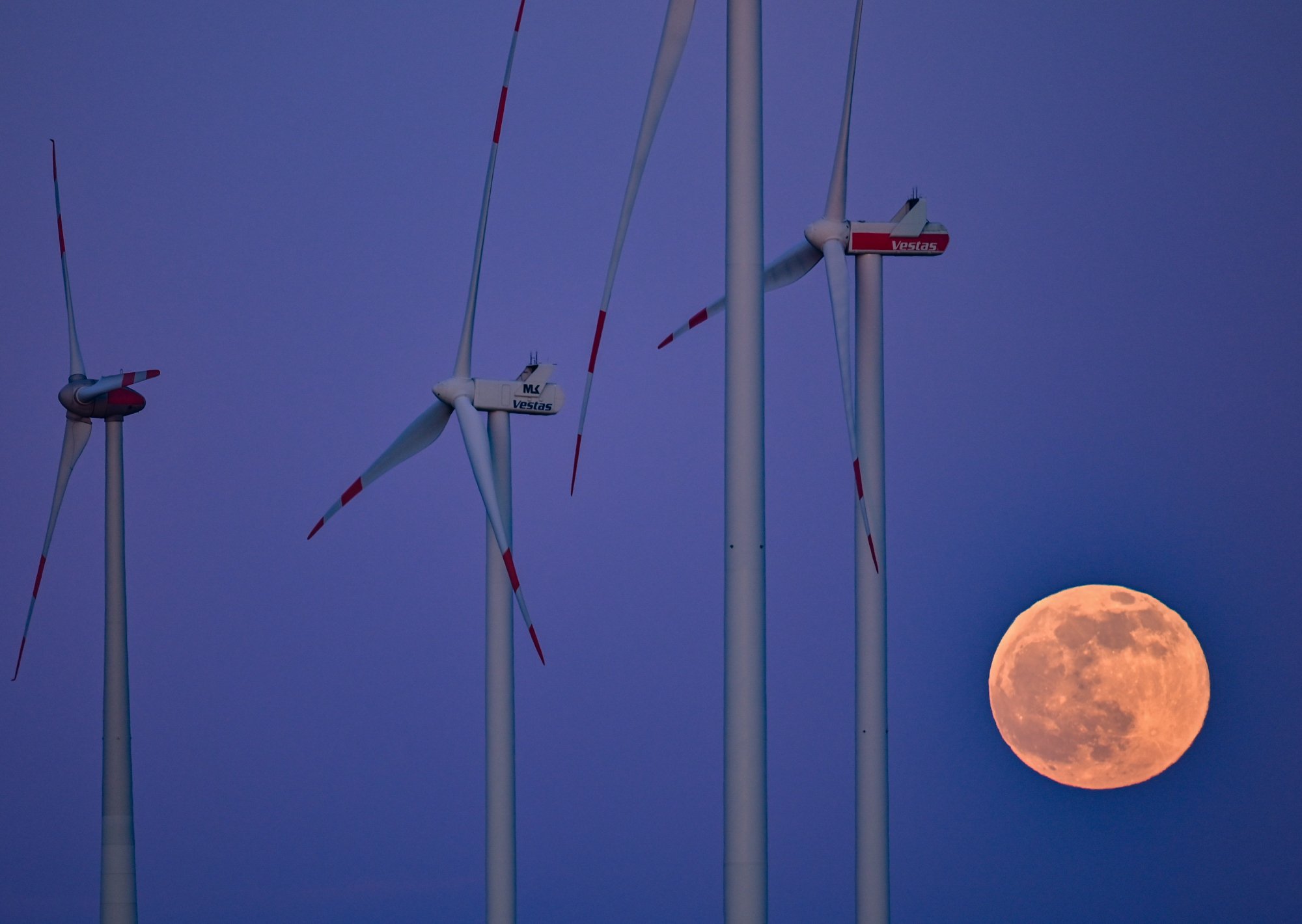 A pink-tinged moon beside wind turbines.