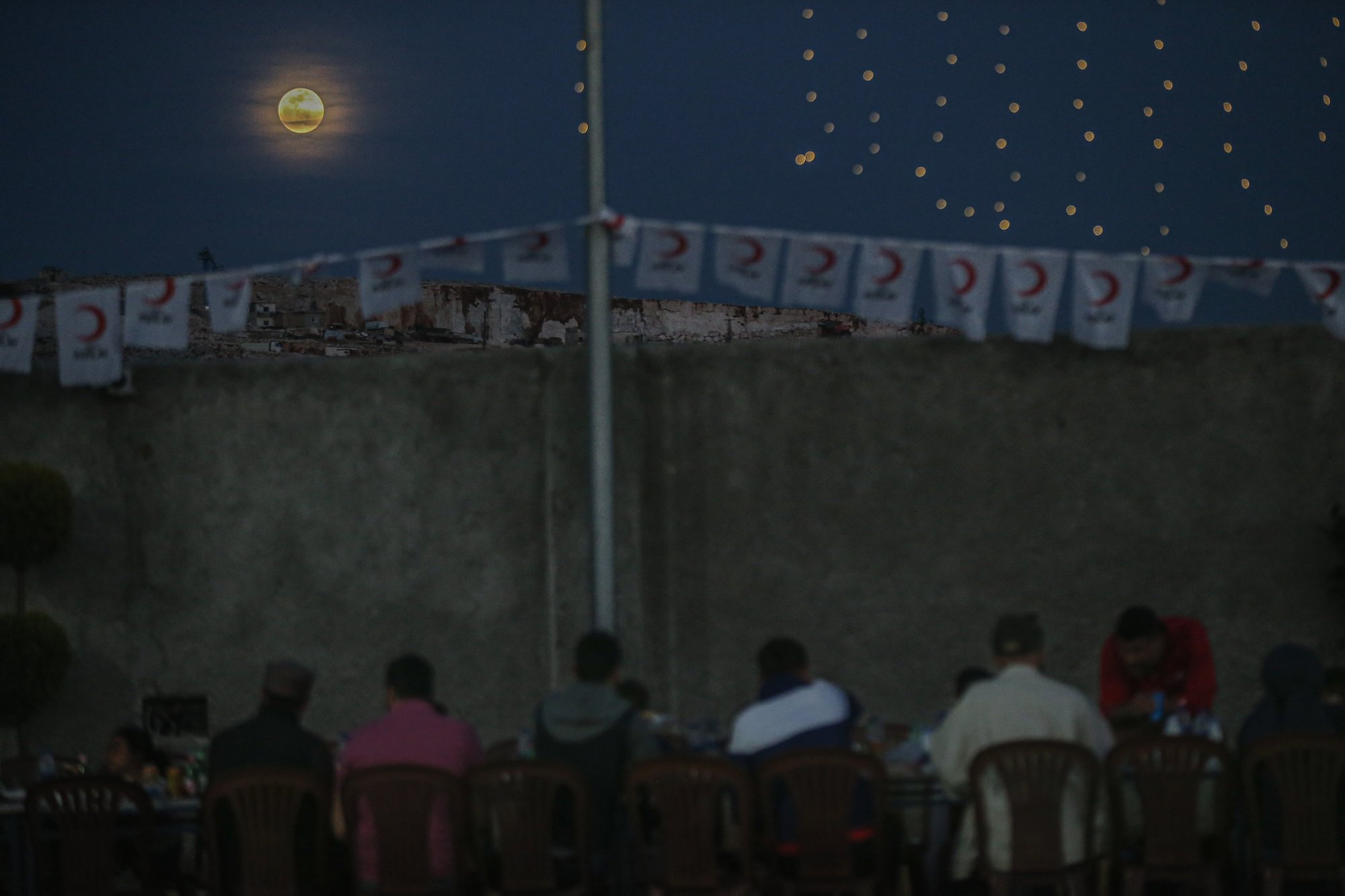 The moon above people sitting at a table with crescent moon flags.