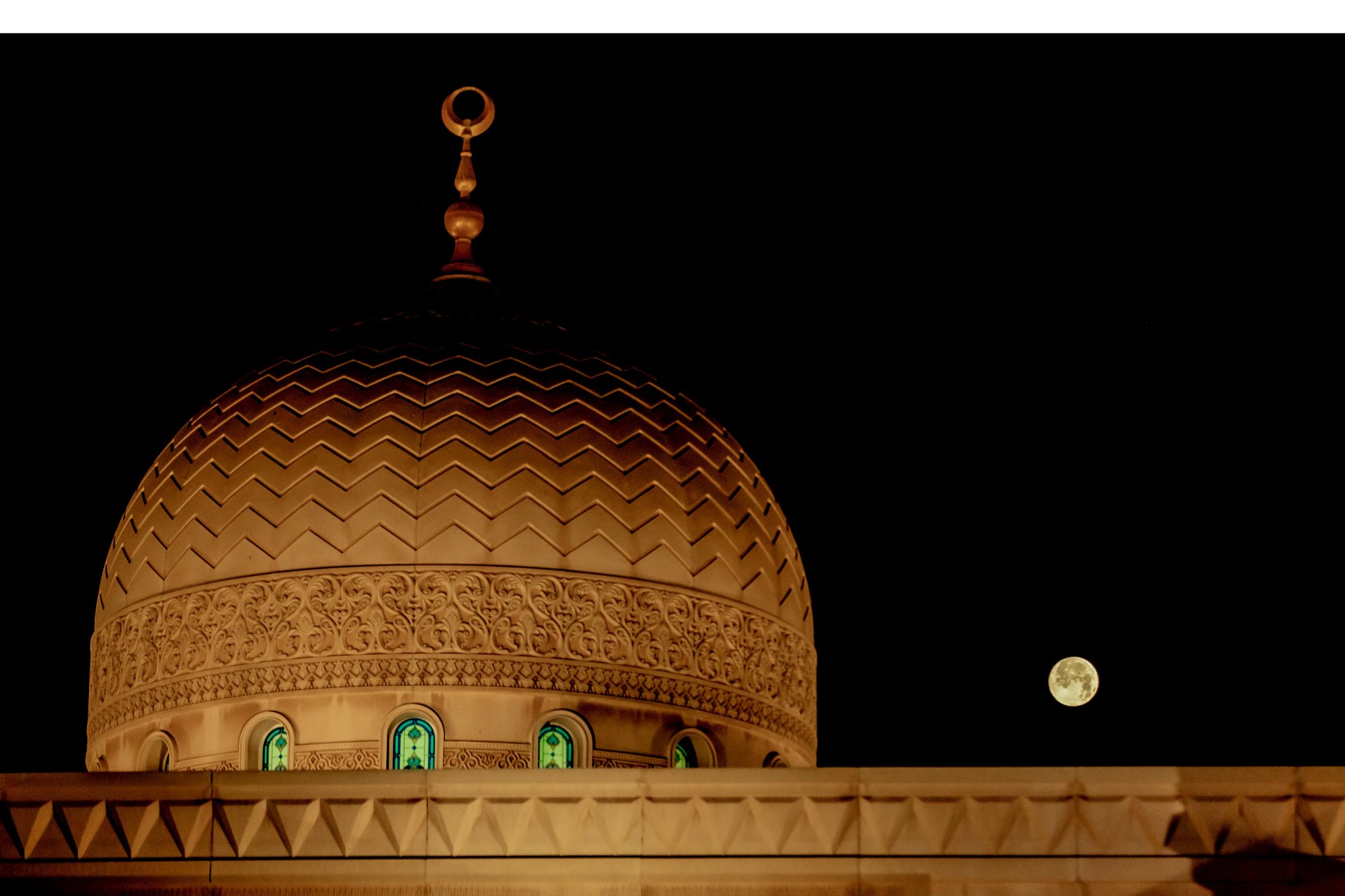 A gold tinged full moon beside a domed building. 