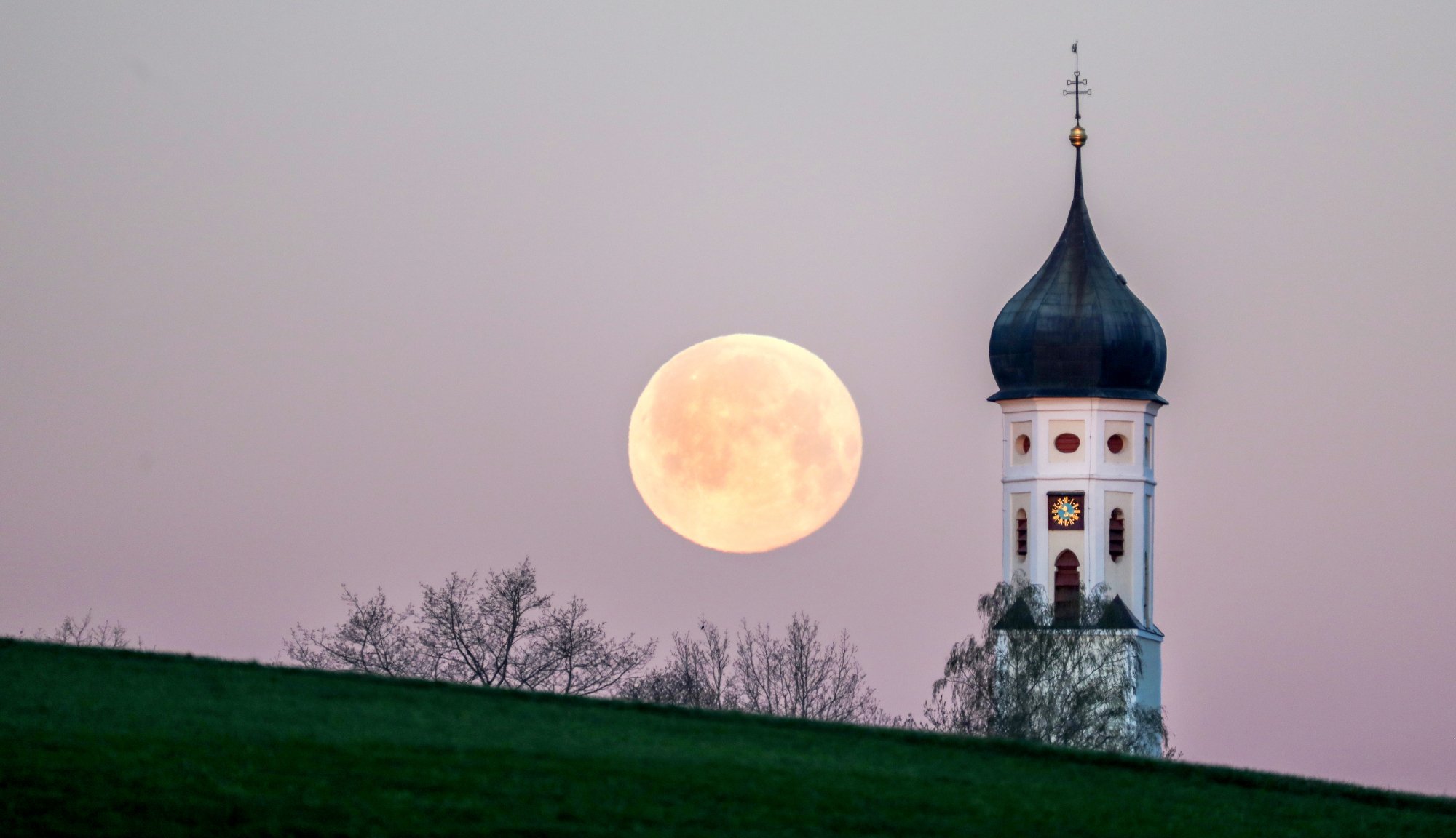 The full moon beside a Church spire.