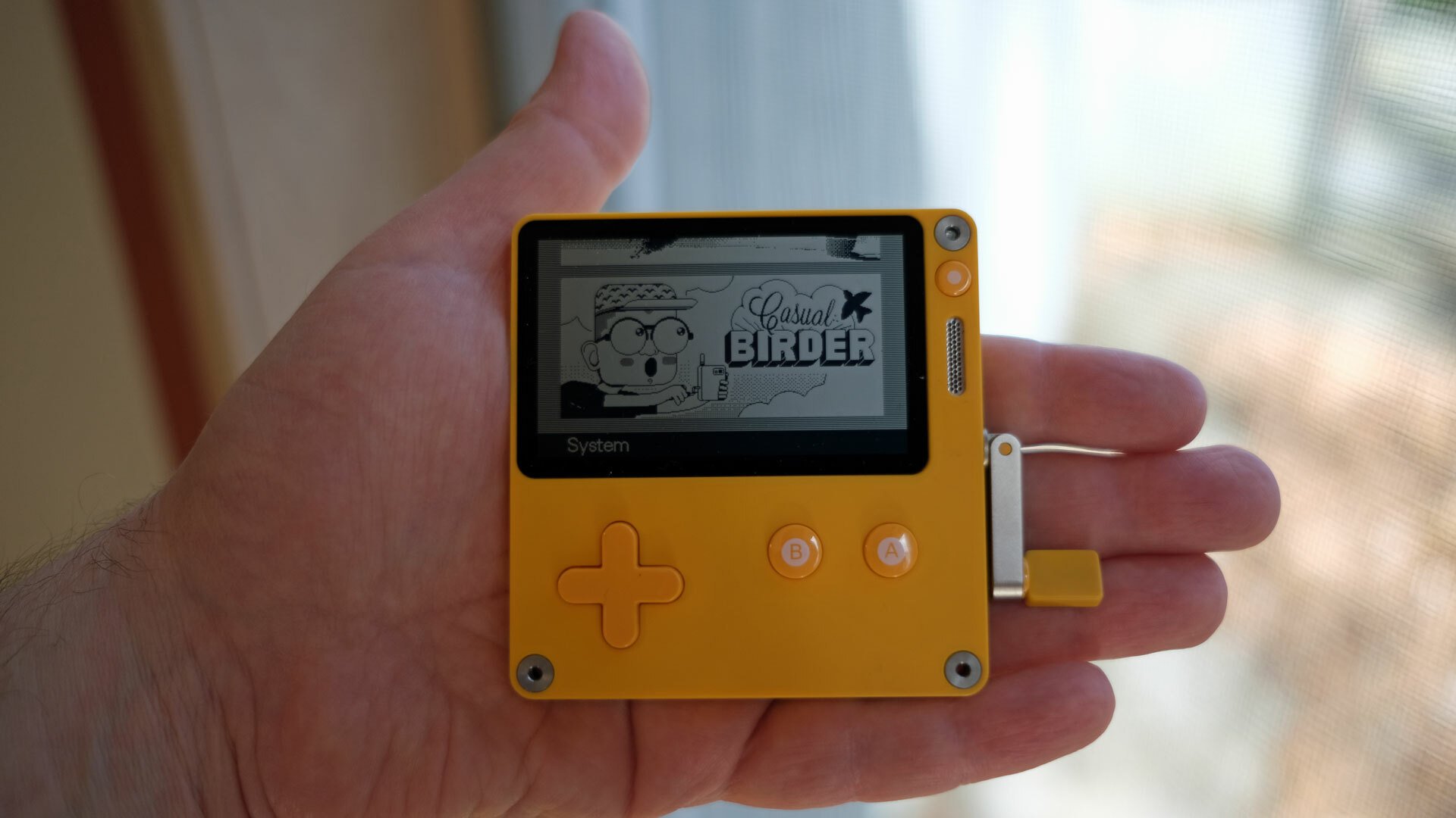 A Playdate gaming device clutched in someone's palm.