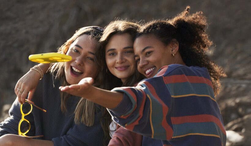 Three young women look at a yellow drone in front of them.