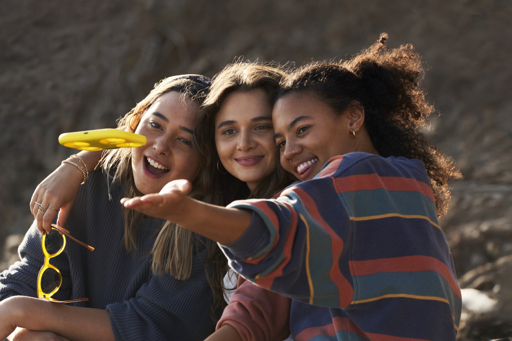 Three young women look at a yellow drone in front of them.