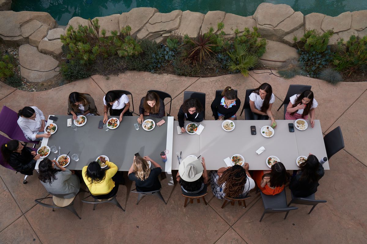 Sixteen women dining around an outdoor table, as seen from above.